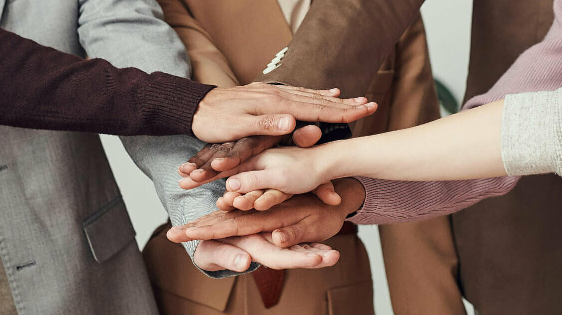 Symbolbild für eine gemeinsame Resolution: Sechs Menschen halten ihre Hände übereinander